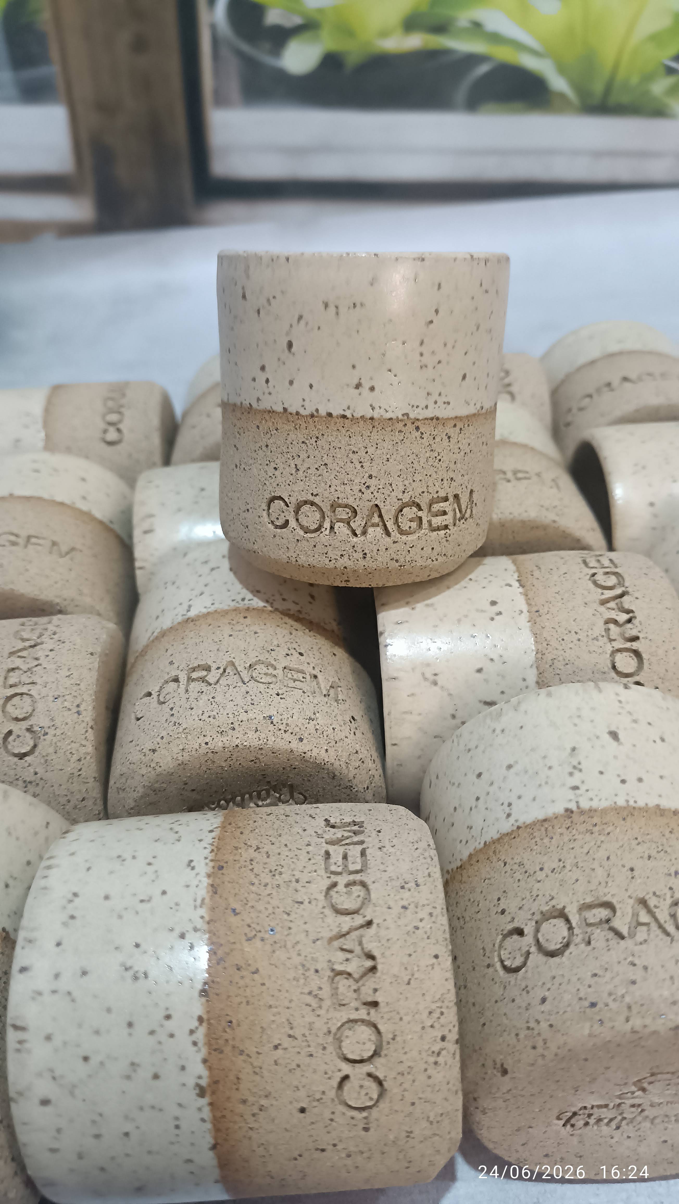 Copos de cerâmica com palavras como coragem e abraços gravadas